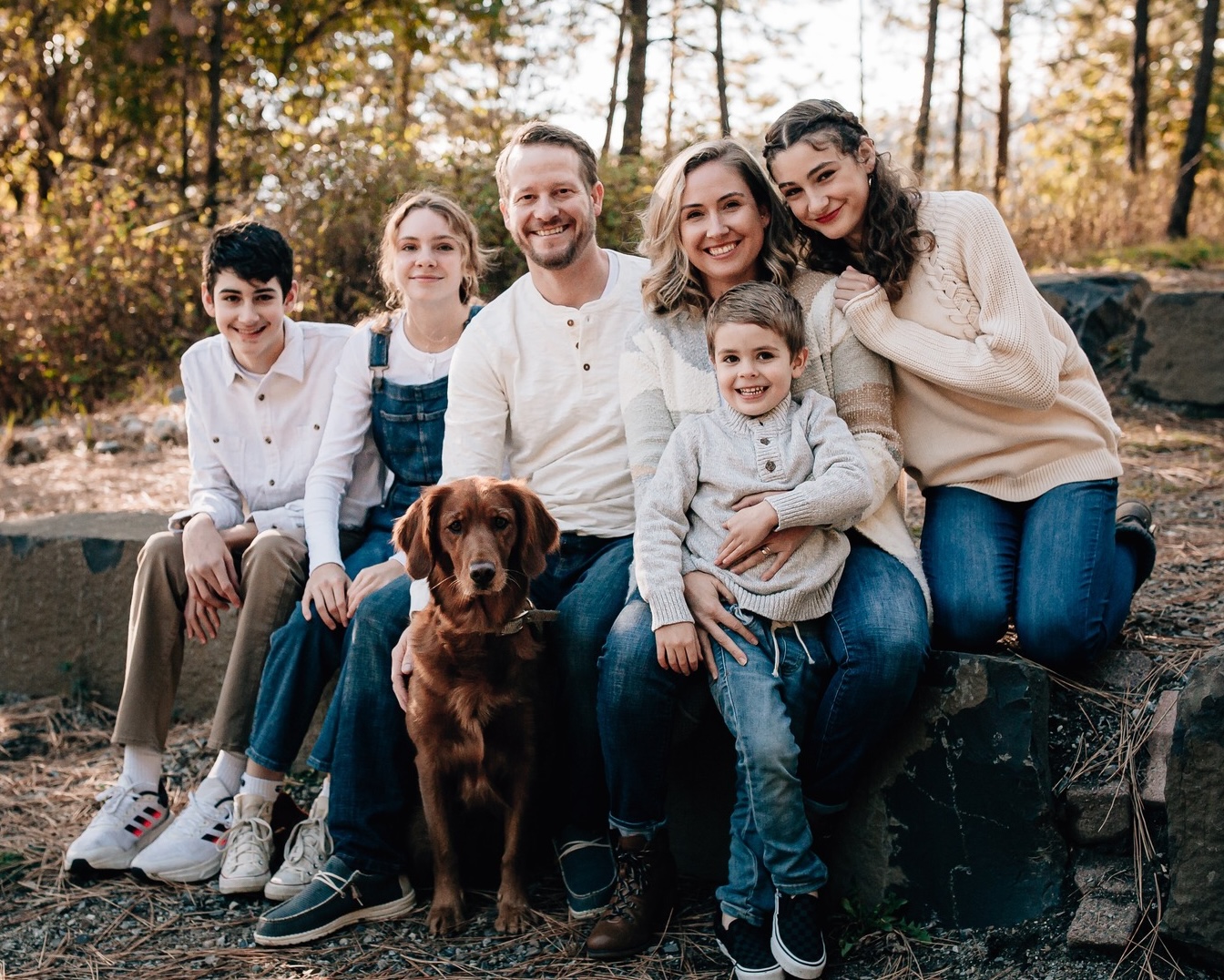 Joshua Cypher with his wife, four kids, and the family dog, sitting on a rock outside in the woods